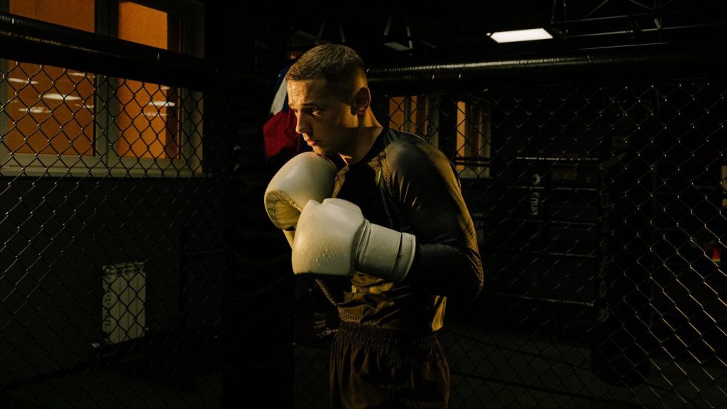 Focused boxer practicing in a dim-lit gym cage, showcasing determination and skill.