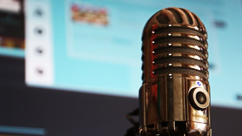 Vintage microphone in focus against a blurred computer screen background.