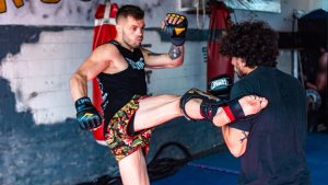 Two men engaged in a dynamic kickboxing training inside a gym.