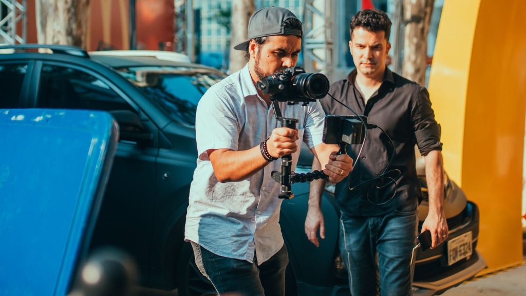 Two men managing a film shoot with camera stabilizer outdoors, showcasing professional gear handling.