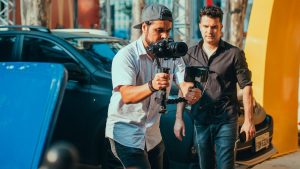 Two men managing a film shoot with camera stabilizer outdoors, showcasing professional gear handling.