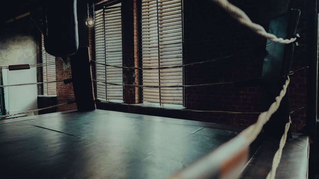 Empty boxing ring in an atmospheric gym with moody lighting and brick walls.