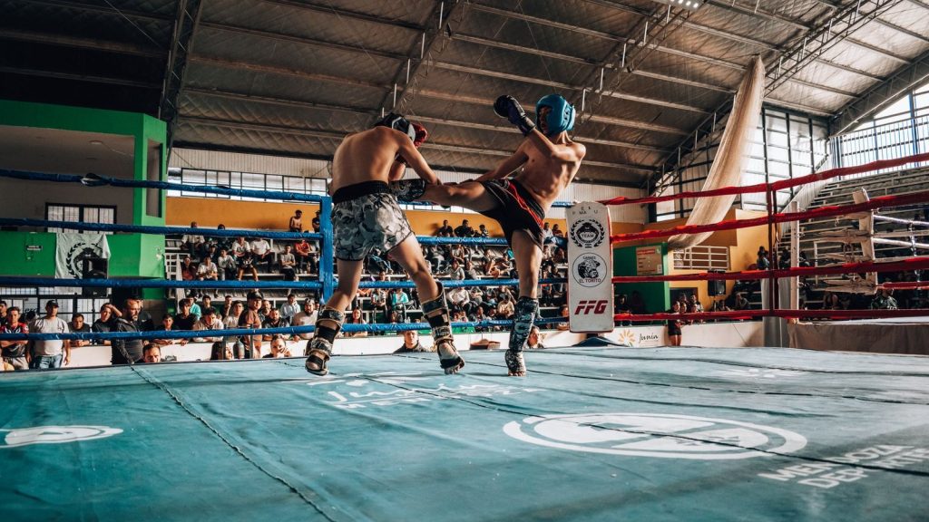 Two athletes engaged in high-energy kickboxing match in a packed indoor arena.