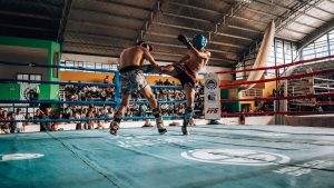 Two athletes engaged in high-energy kickboxing match in a packed indoor arena.