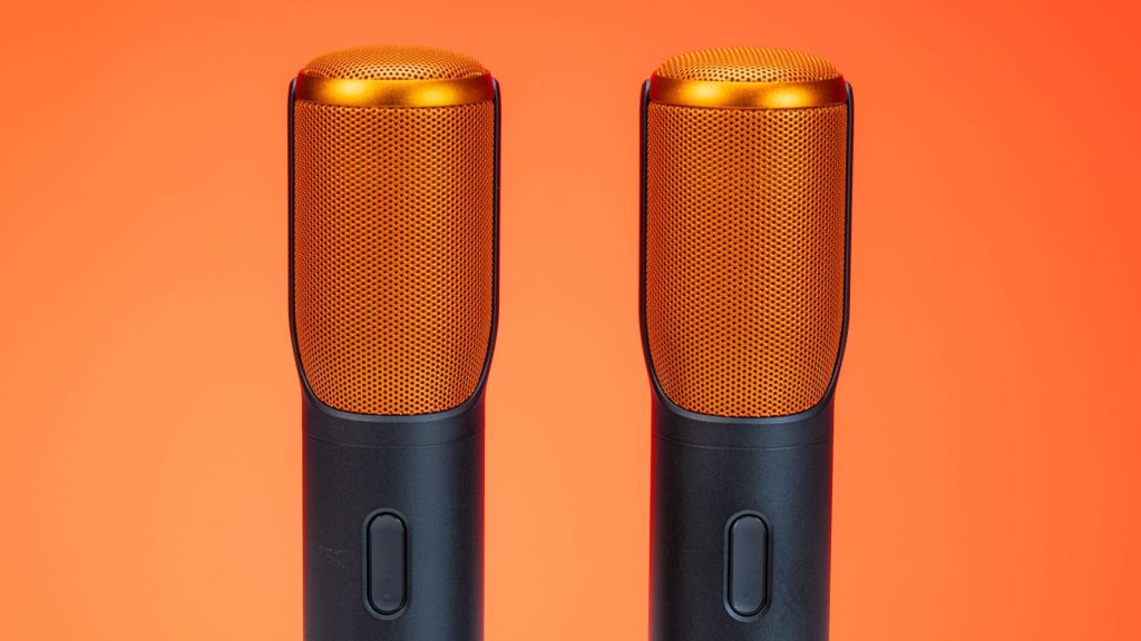 Vibrant photo of two modern microphones against an orange background, highlighting technology.