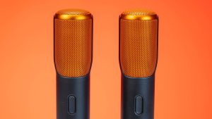Vibrant photo of two modern microphones against an orange background, highlighting technology.