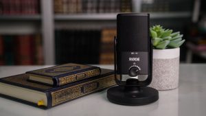 Close-up of books with a Røde microphone and succulent on a desk.