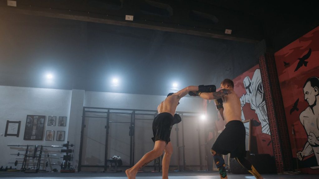 Two men engaged in a powerful kickboxing training session indoors, showcasing strength and agility.