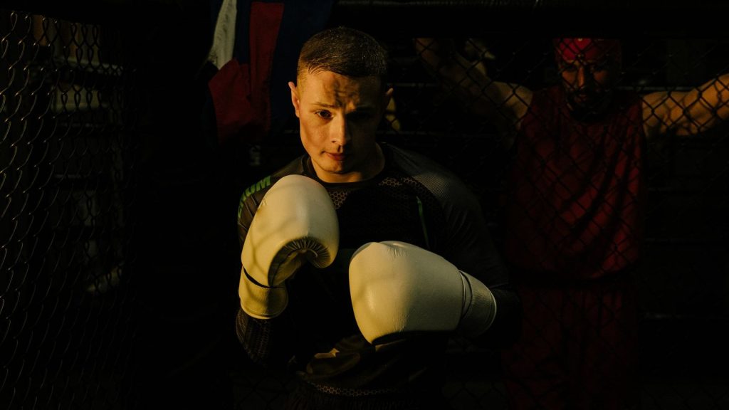 Focused boxer with gloves ready for sparring inside dimly lit training cage.