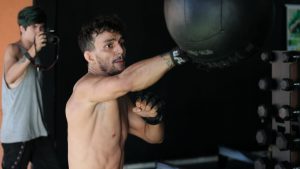 A boxer throws a punch at a heavy bag while training indoors with a camera crew.