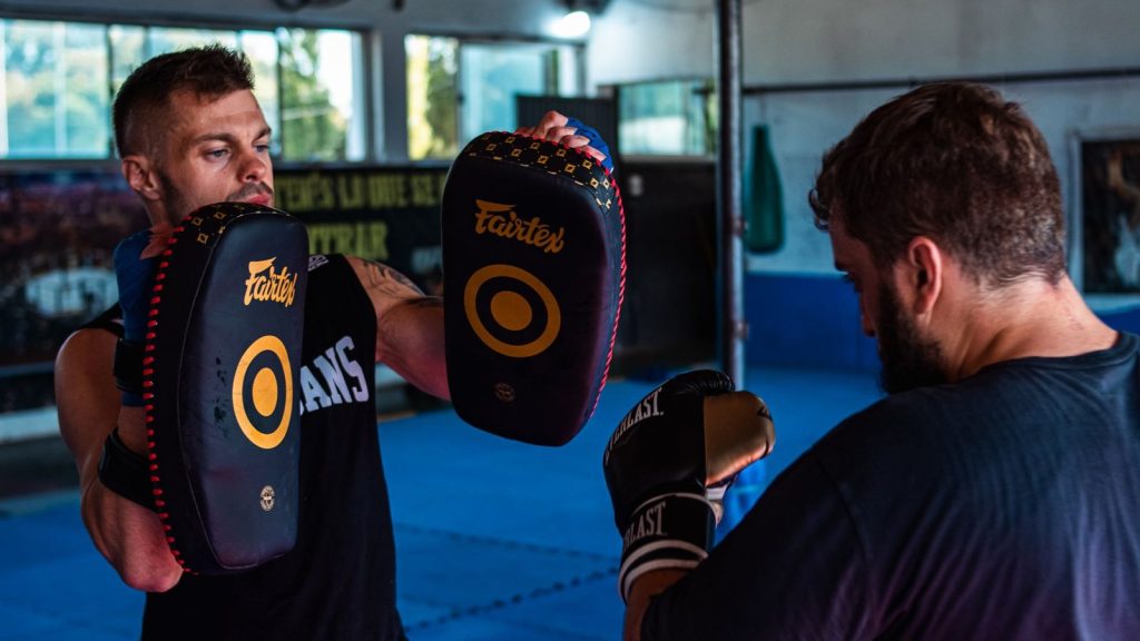 Two men practicing kickboxing with focus pads in a gym, showcasing agility and strength.