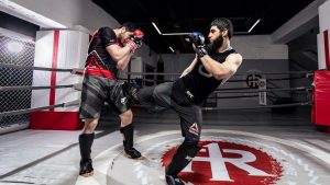 Two men practicing kickboxing in a gym, showcasing martial arts skills in a training ring.