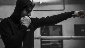 Black and white image of a boxer in a hoodie practicing punches in a boxing ring.