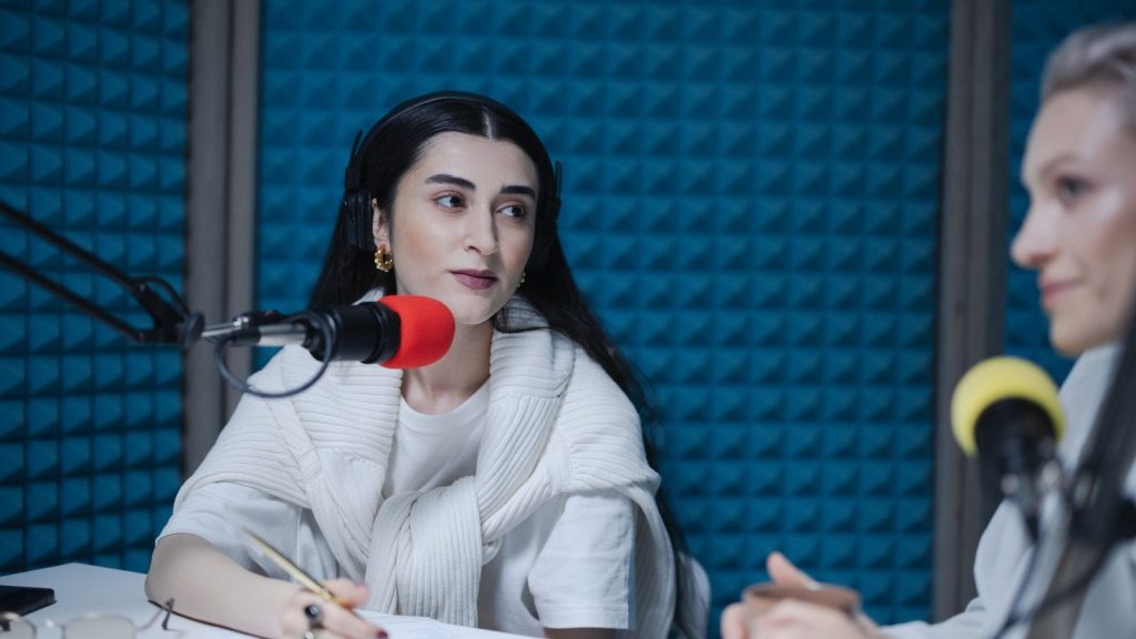 Two women engaged in a podcast recording with professional microphones, soundproof studio.