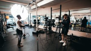Behind the scenes of a fitness documentary being filmed in a gym with professional lighting equipment.