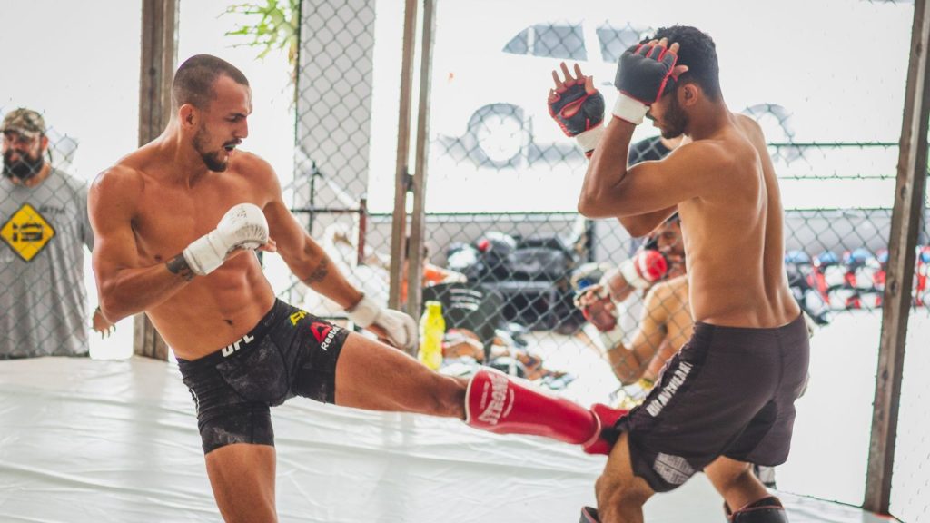 Two fighters practicing kicks and defense in a gym, showcasing martial arts skills.
