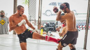 Two fighters practicing kicks and defense in a gym, showcasing martial arts skills.