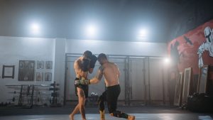 Two men engaged in an intense MMA training session inside a gym under dramatic lighting.