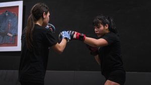 Two women practice boxing techniques in a gym, focusing intently.