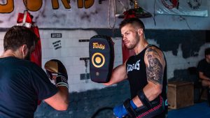 Two men engaged in a focused boxing training session indoors with gear.