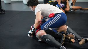 Two men engage in a martial arts sparring session on a gym mat, showcasing intense training.