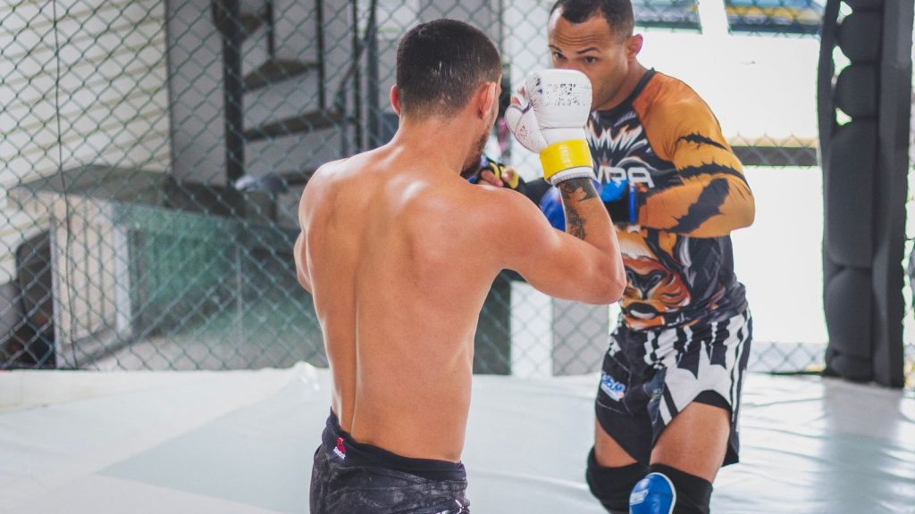 Two men engaging in martial arts sparring session indoors, showcasing intense training.