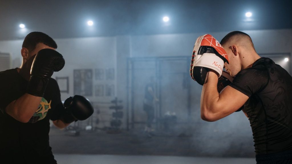 Two men sparring in an indoor gym, focusing on boxing techniques and fitness.