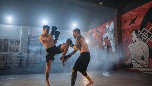 Two athletes engaged in an intense MMA sparring session inside a gym with striking wall art.
