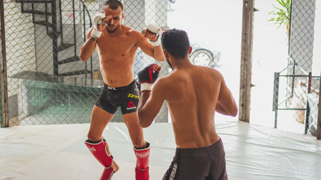 Two men practicing mixed martial arts sparring in a gym's cage.