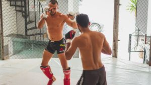 Two men practicing mixed martial arts sparring in a gym's cage.