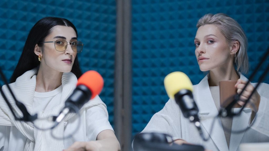 Two women in a soundproof studio with microphones, recording a podcast.