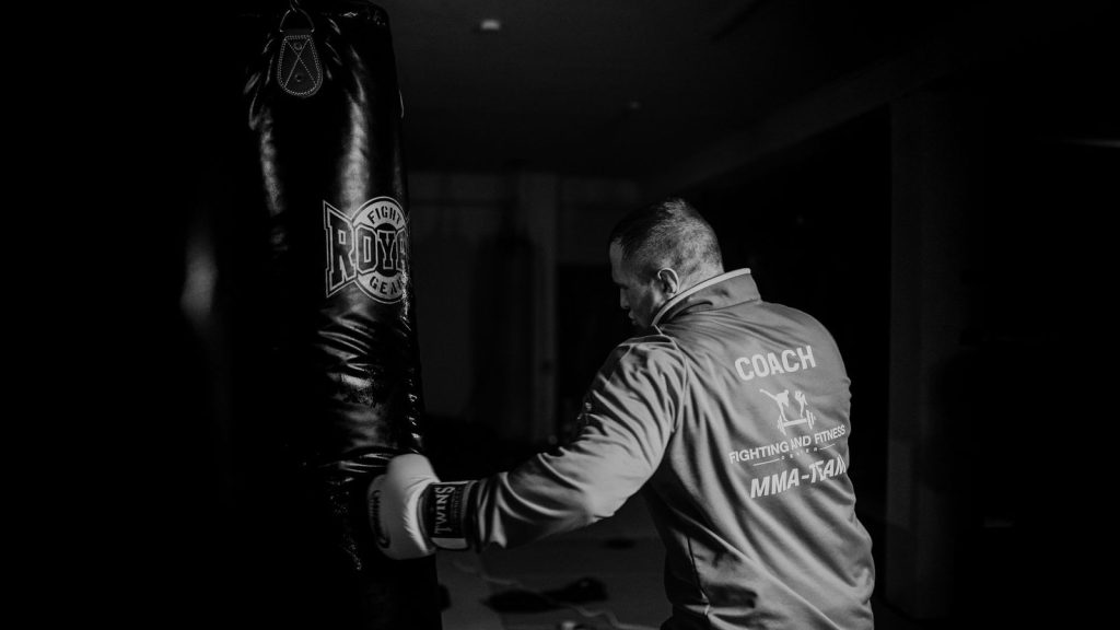 A boxing coach practicing punches on a heavy bag indoors, showcasing strength and focus.