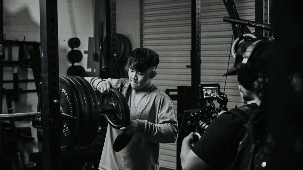 A man focuses while adjusting weights in a gym during weightlifting session captured in monochrome.