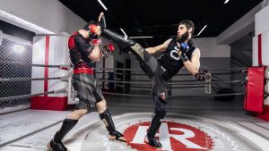 Two men practicing kickboxing in a gym, showcasing intense training and martial arts skills.