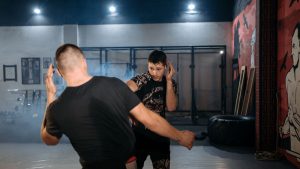 Two men engage in a dynamic martial arts sparring session at an indoor gym.