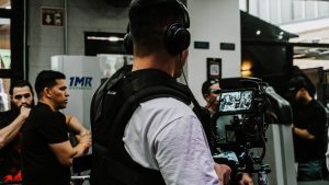 Back view of a filmmaker using a camera rig indoors with a focus on capturing event activities.
