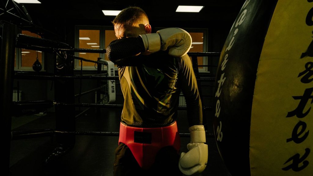 Male boxer in a gym wiping sweat with boxing gloves after training session.