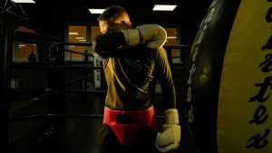Male boxer in a gym wiping sweat with boxing gloves after training session.