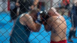 Two men engaged in a boxing match inside a caged ring, showcasing martial arts and sportswear.