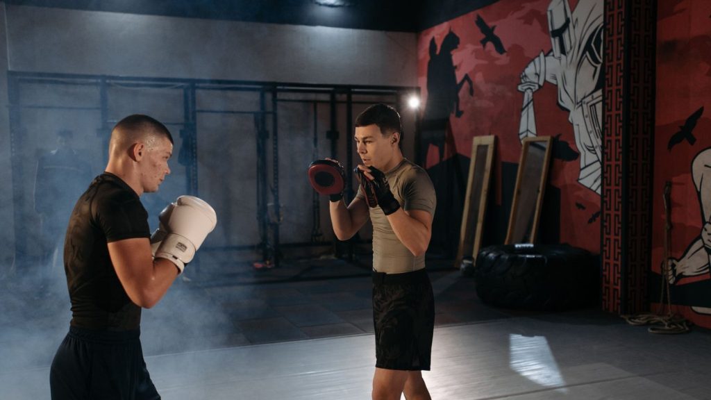 Two men engaged in an intense MMA training session indoors with boxing gear.