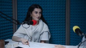 A woman in a podcast studio with microphones and headphones, focused on a discussion.
