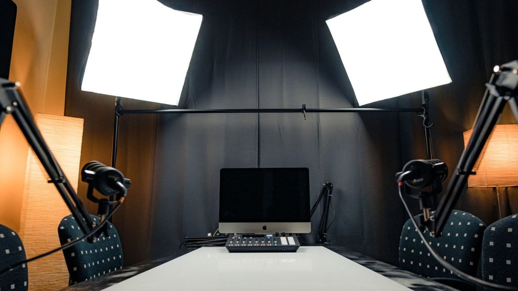 A modern podcast recording studio with microphones, lighting, and computer equipment.