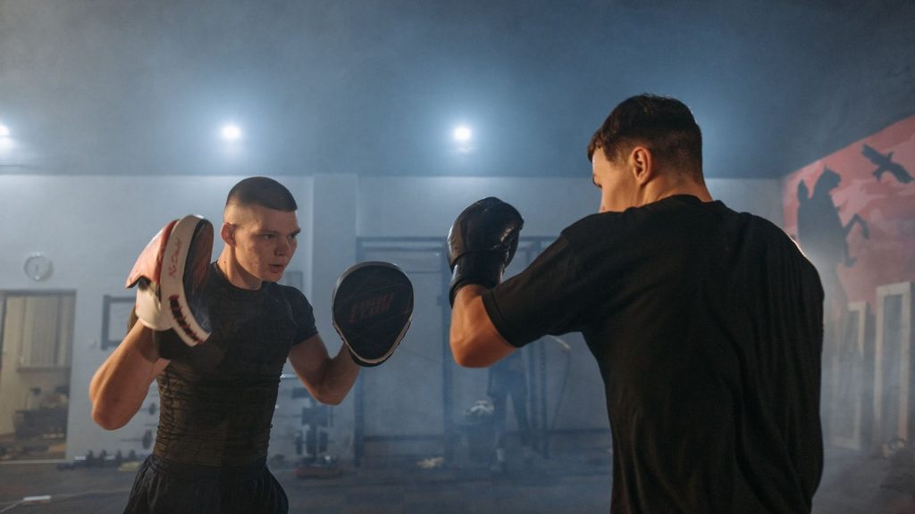 Two men engaged in boxing training indoors, showcasing focus and athleticism.