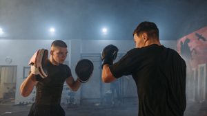 Two men engaged in boxing training indoors, showcasing focus and athleticism.