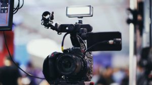 A close-up shot of a Canon video camera with attached equipment in a blurred indoor setting.