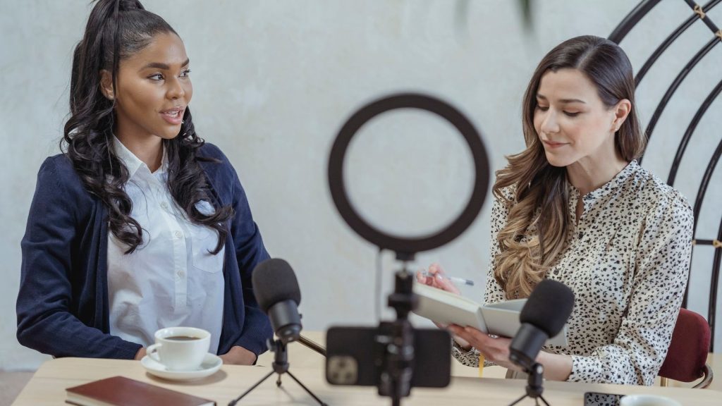 Two women conducting a podcast interview with microphones and coffee.