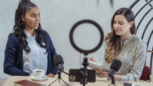 Two women conducting a podcast interview with microphones and coffee.
