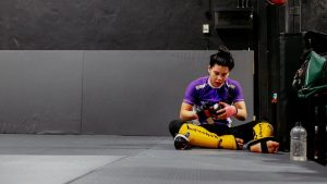 A female martial artist sits on the gym floor during a break. Focused and ready.