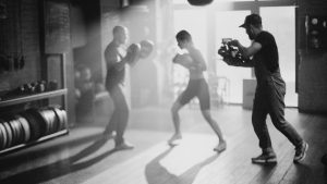 Black and white image capturing a boxing training session with a cameraman filming.
