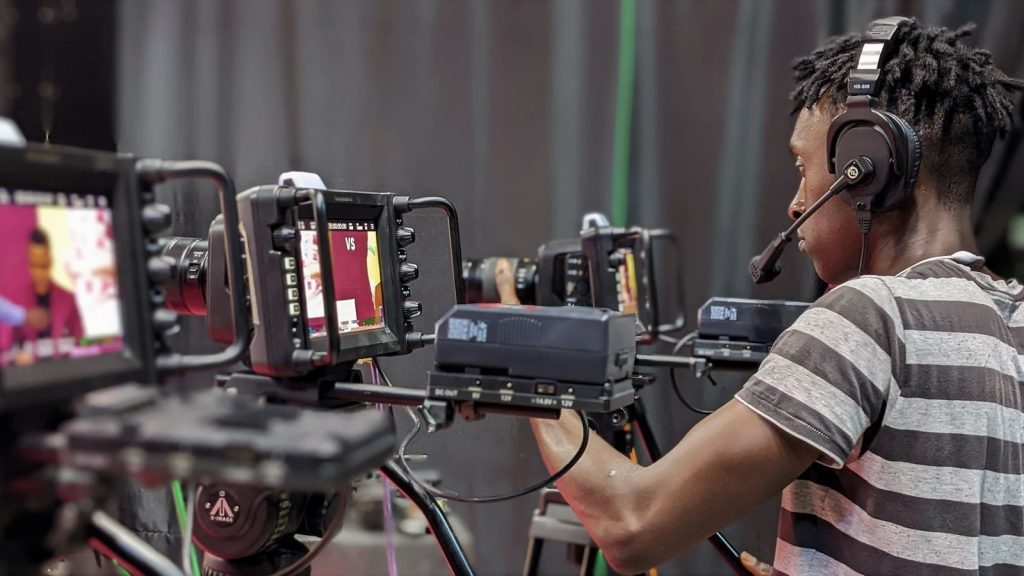 A videographer adjusts camera equipment during a live broadcast in a studio setting.